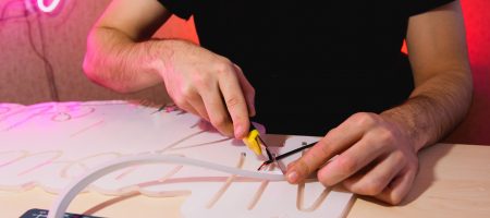 Cropped view of man cutting flex neon stripe near signboard in workshop